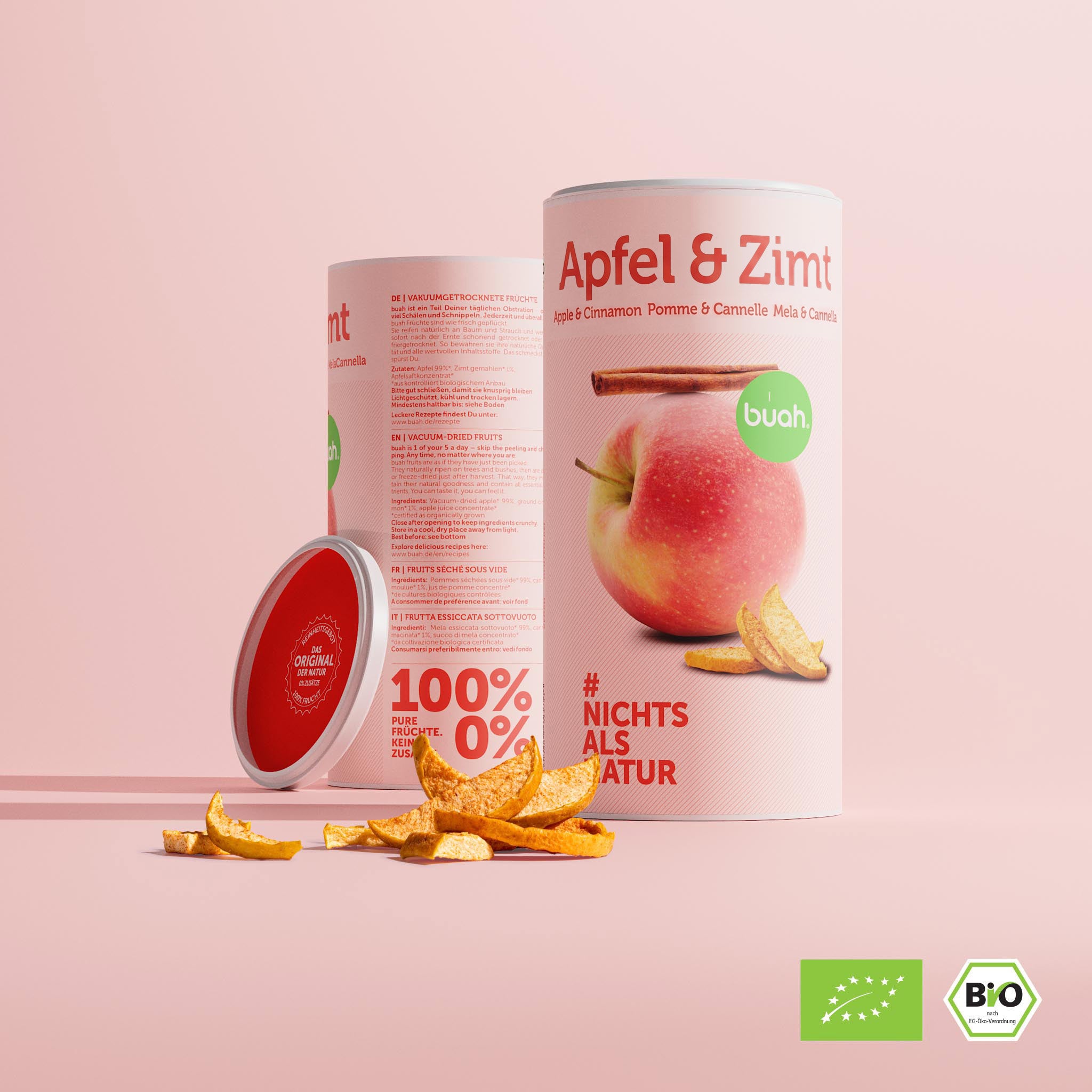 Eine große Dose buah gefriergetrocknete Früchte der Sorte Apfel & Zimt steht vor einem rosa Hintergrund. Dahinter steht eine zweite Dose, die ihre Rückseite mit den Zutaten zeigt. Ein roter Deckel lehnt seitlich an. Im Vordergrund liegen Apfelstücke.