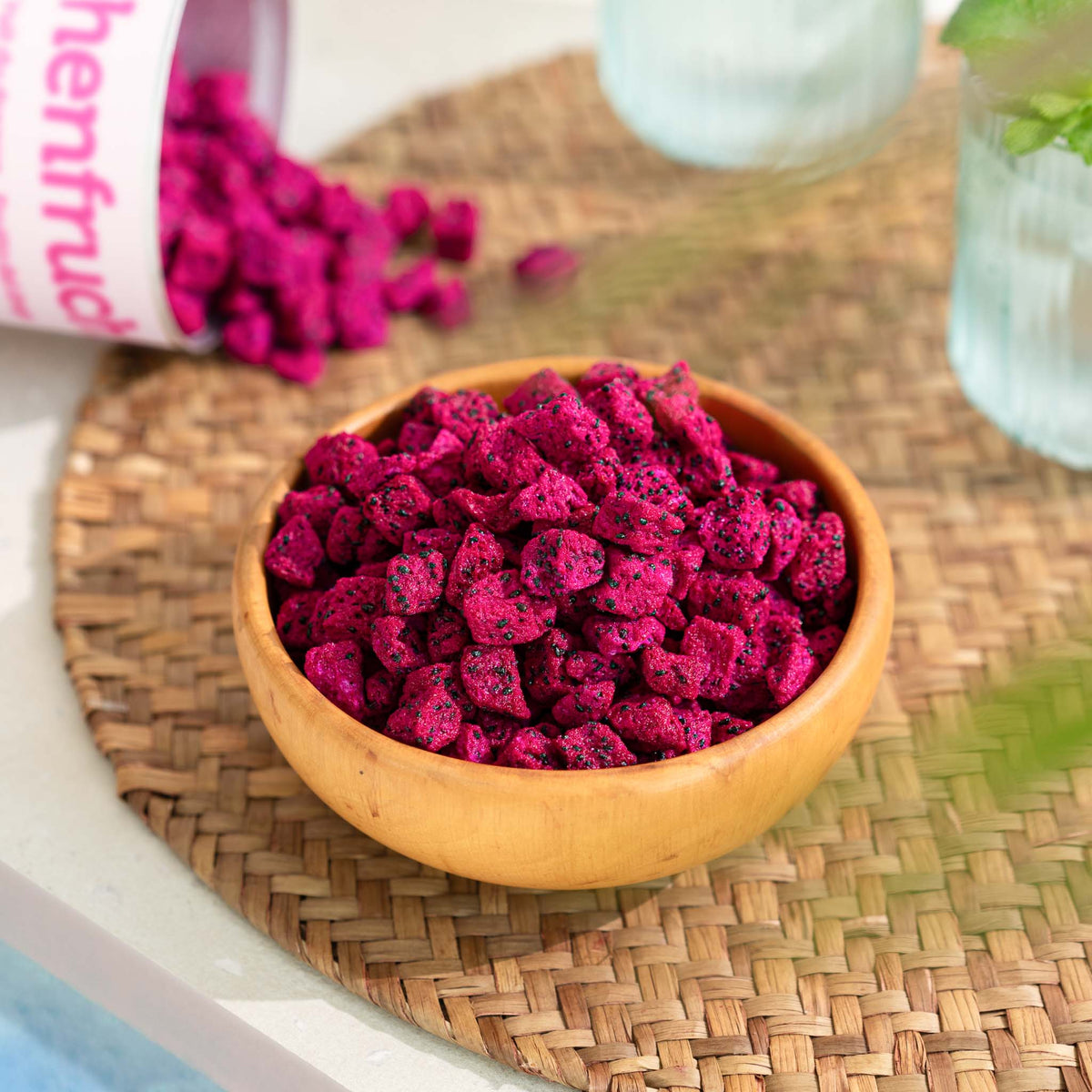Holzschale voll mit Wuerfel buah gefriergetrockneter Drachenfrucht in satter pinker Farbe auf einem Tisch