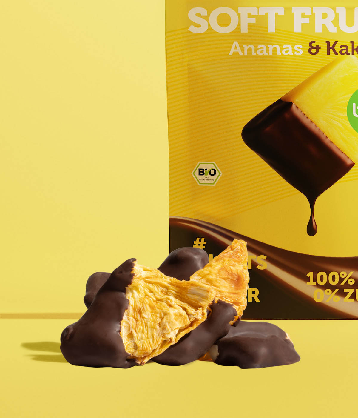 Getrocknete Bio-AnanasstĂĽcke mit dunklem Kakaomantel vor der buah Soft Fruits Ananas & Kakao Verpackung