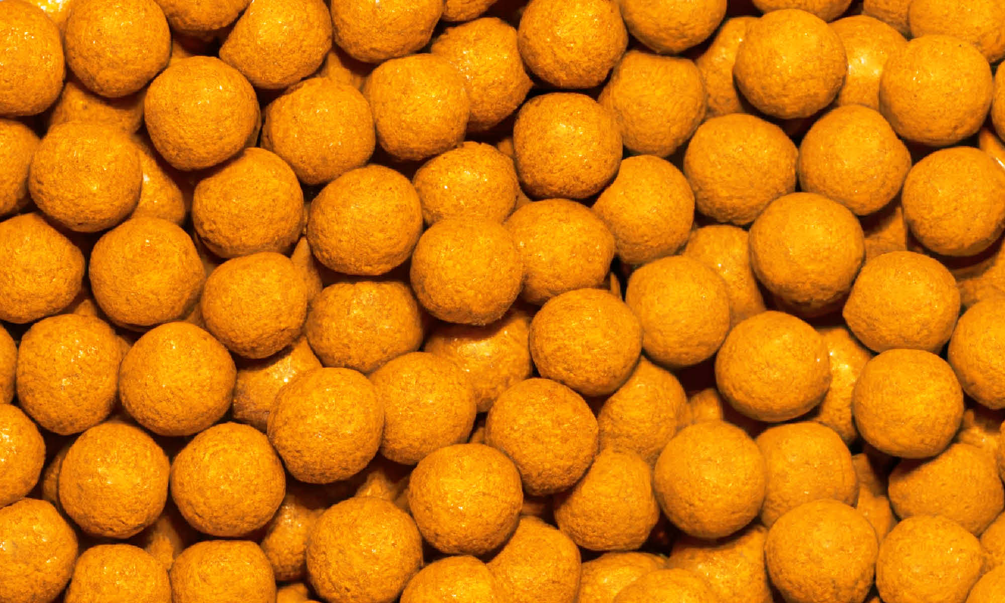 Viele kleine, runde und orangene buah Mango-Kokos Kaubonbons neben und aufeinander 
