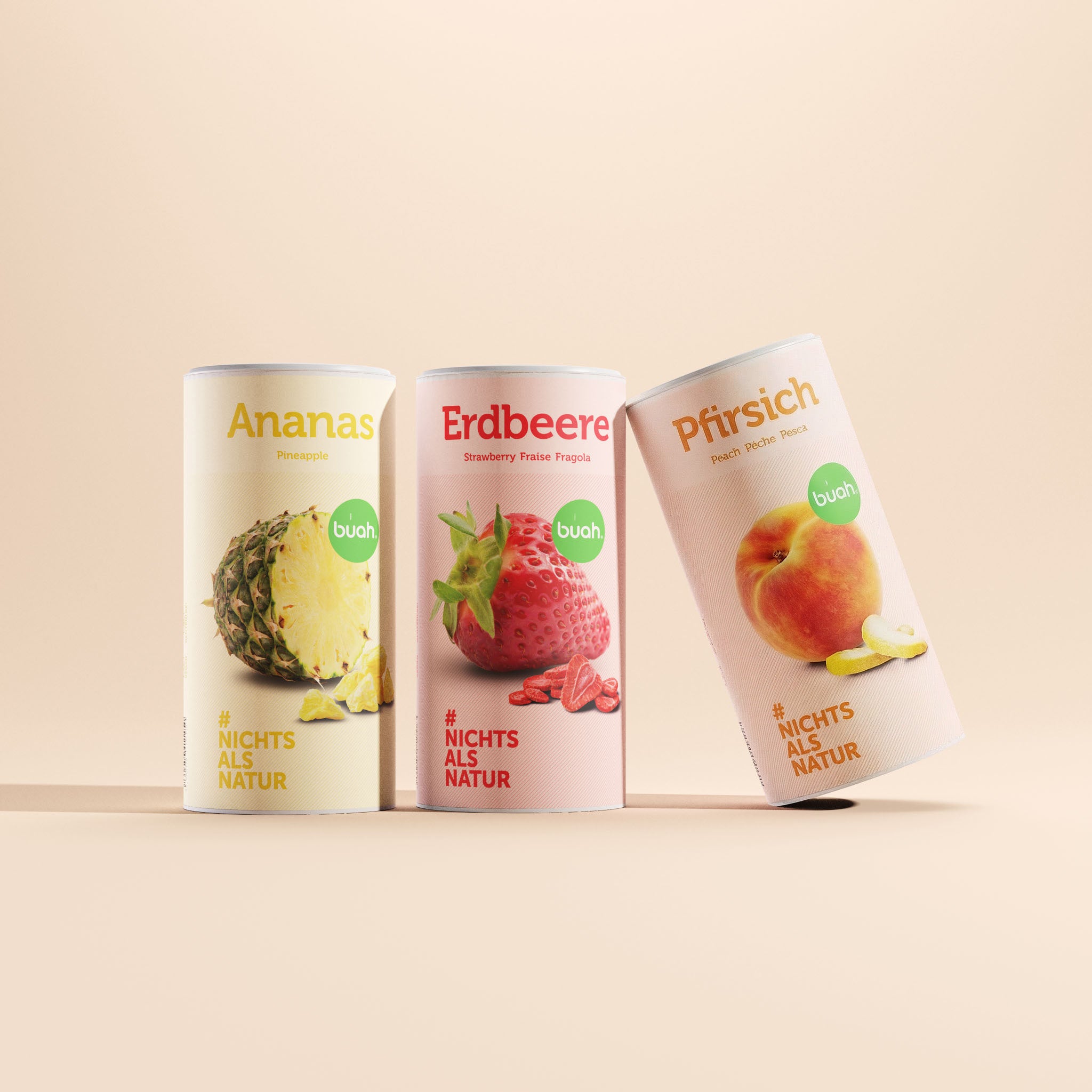 buah Refresh-Set. Drei große Dosen buah gefriergetrocknete Früchte in den Sorten Ananas, Erdbeere und Pfirsich stehen vor einem beigefarbenen Hintergrund. Die rechte Dose mit der Sorte Pfirsich ist leicht nach rechts gekippt.