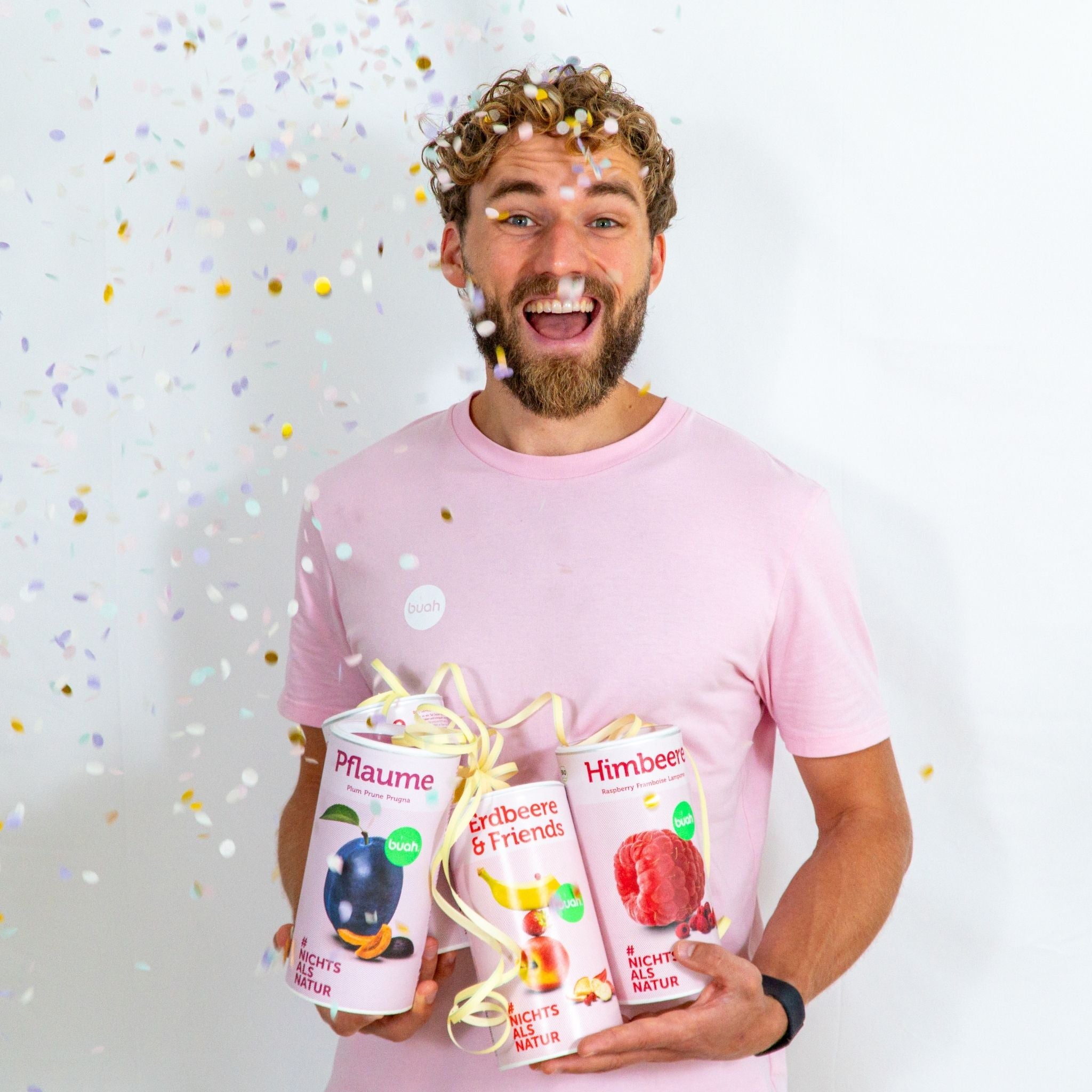 Daniel Gruender von buah in rosa buah Shirt mit buah gefriergetrockneten Fruechten in der Dose im Arm - Konfetti und Luftschlangen im Hintergrund  fuer den buah Birthday