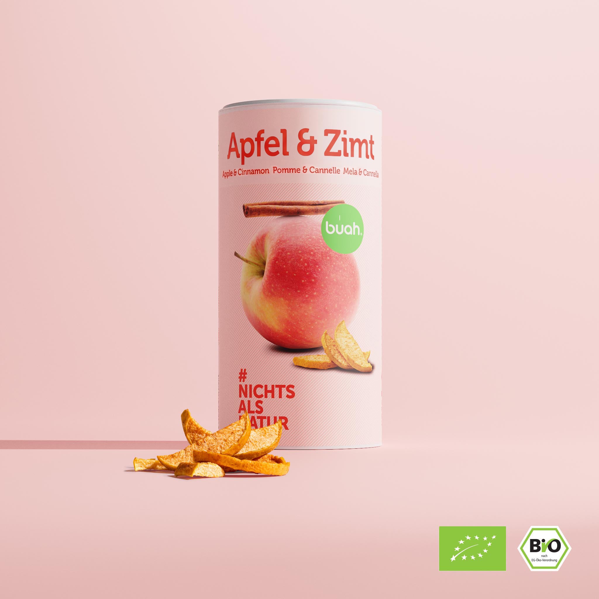 Eine große Dose buah gefriergetrocknete Früchte der Sorte Apfel & Zimt steht im Zentrum vor einem rosa Hintergrund. Davor liegen einige knusprige Apfelstücke.